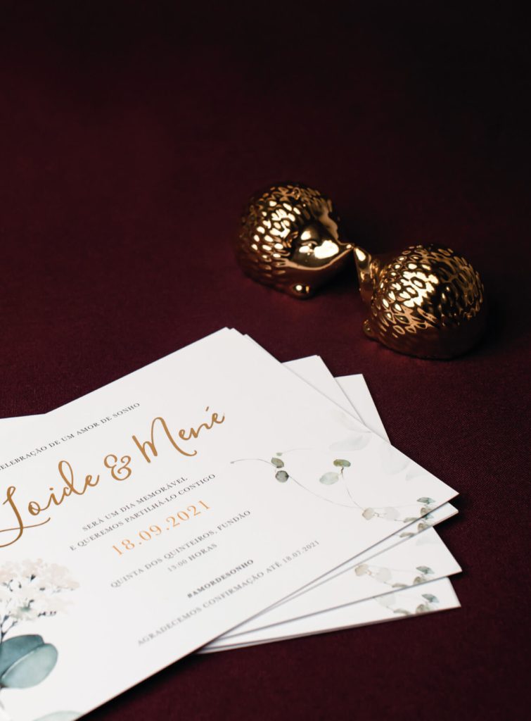 Convite de casamento apresentado sob um fundo vermelho aveludado, com motivos decorativos dourados.