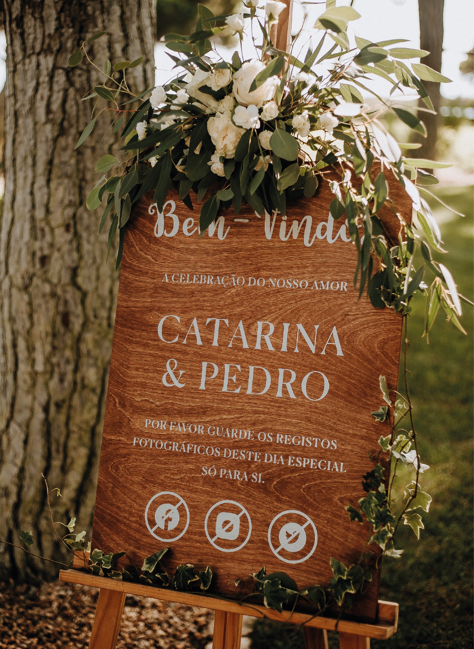 Sinal de boas vindas da atriz Catarina Gouveia feito de madeira com tipografia branca e com flores penduradas