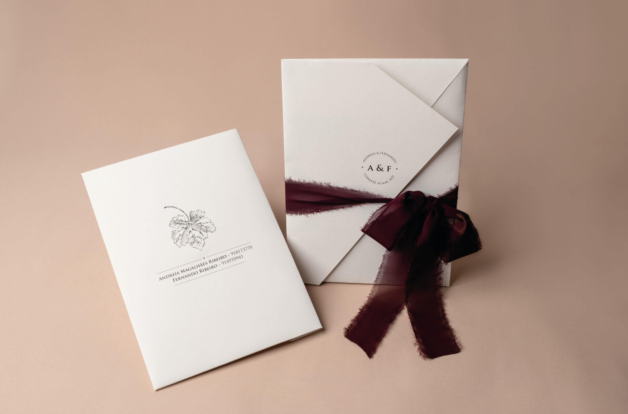 Convites de casamento envoltos de uma tira de tecido bordô, sob um fundo rosa