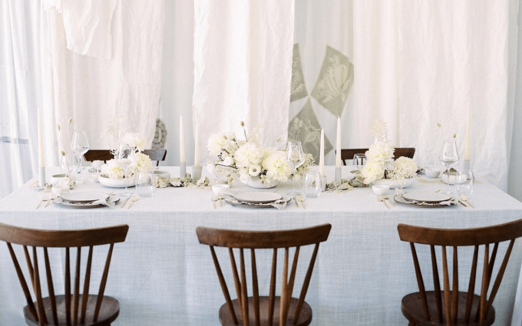 Mesa de casamento branca com pratos e flores brancas com cadeiras de madeira castanhas
