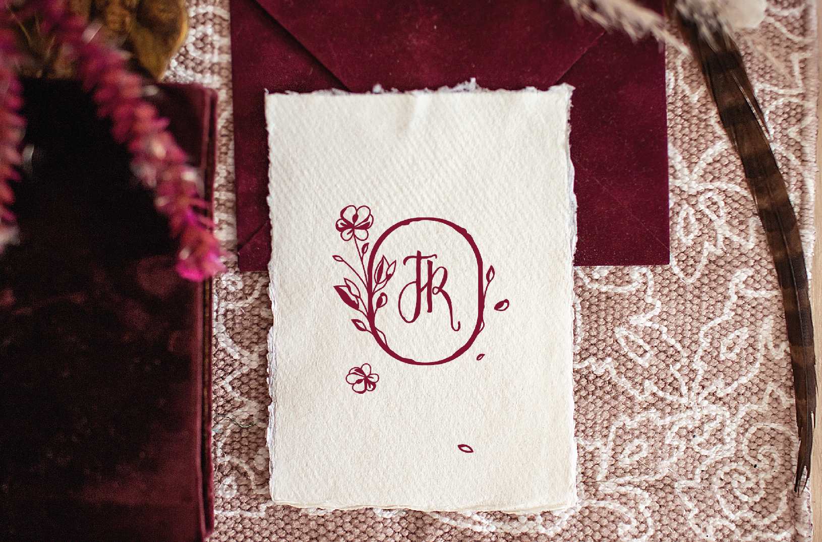 Convite de casamento branco com acabamento rasgado, com flores de cor bordô num fundo rosa velho.