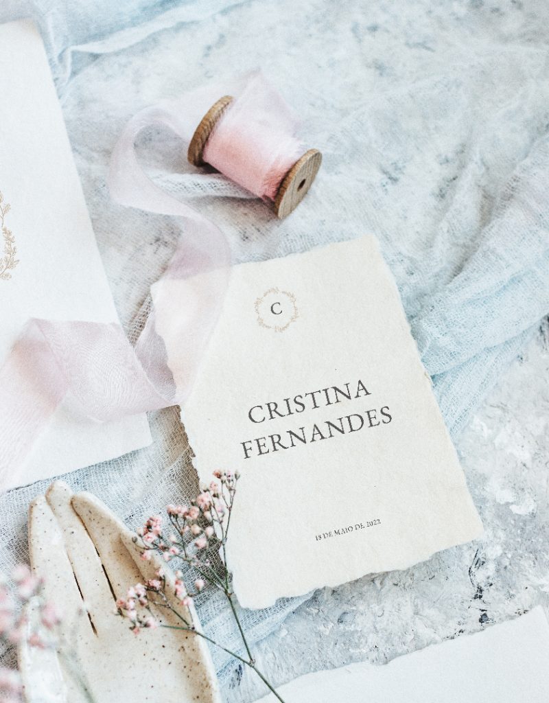 Convite de casamento branco de estilo tipográfico com acabamento rasgado, com fitas rosa e azul e flores rosa