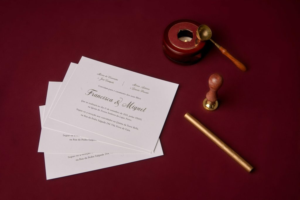 Convite de casamento branco de estilo tipográfico com foil dourado num fundo bordo com material de lacre.