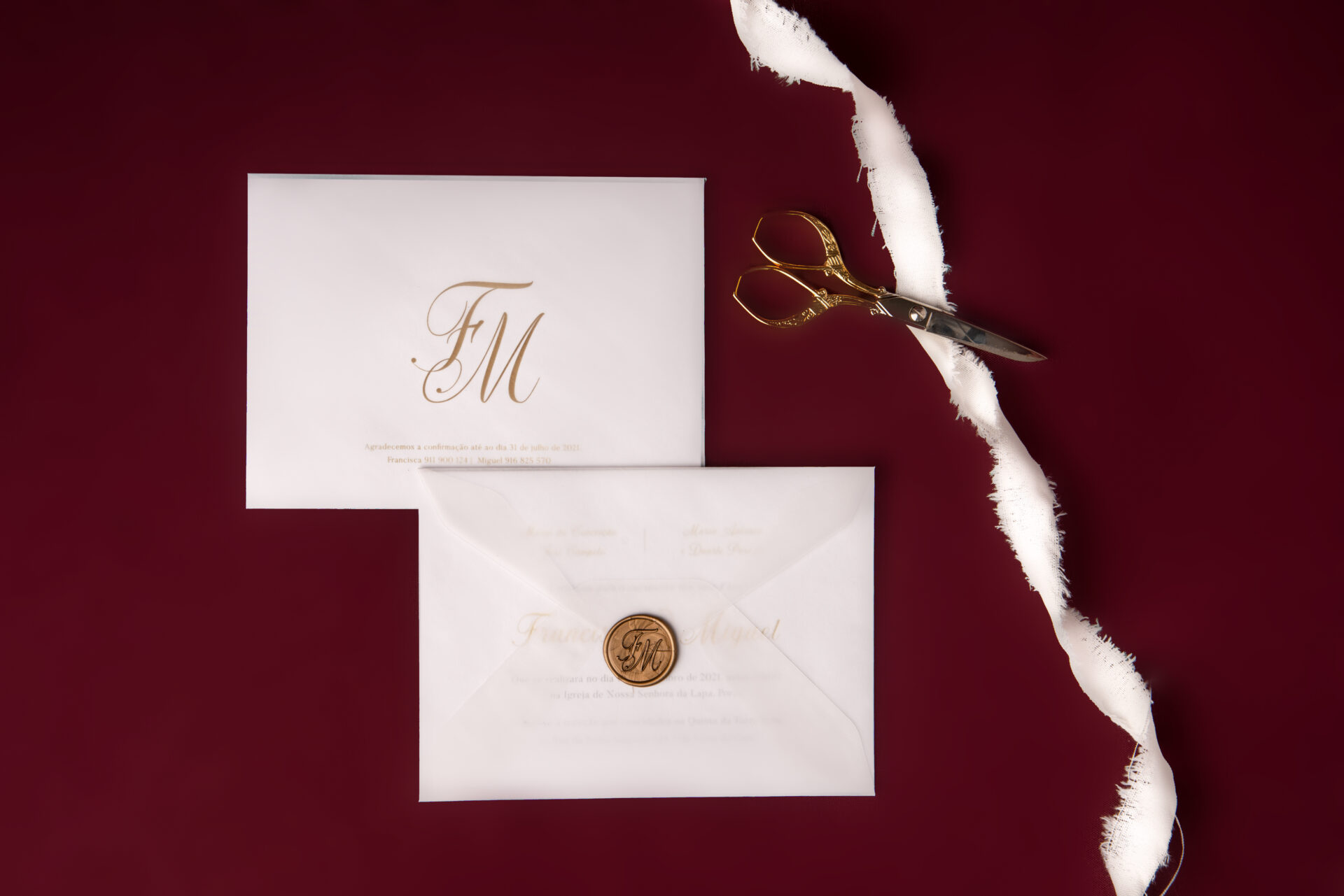 Convite de casamento branco de estilo tipográfico com foil dourado num fundo bordo com uma tesoura dourada