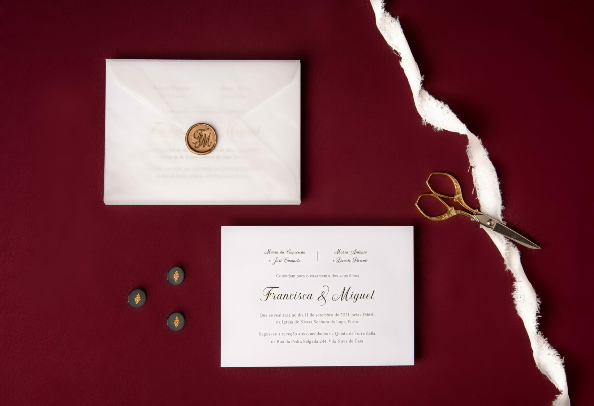 Convite de casamento branco de estilo tipográfico com foil dourado num fundo bordo com uma tesoura dourada.