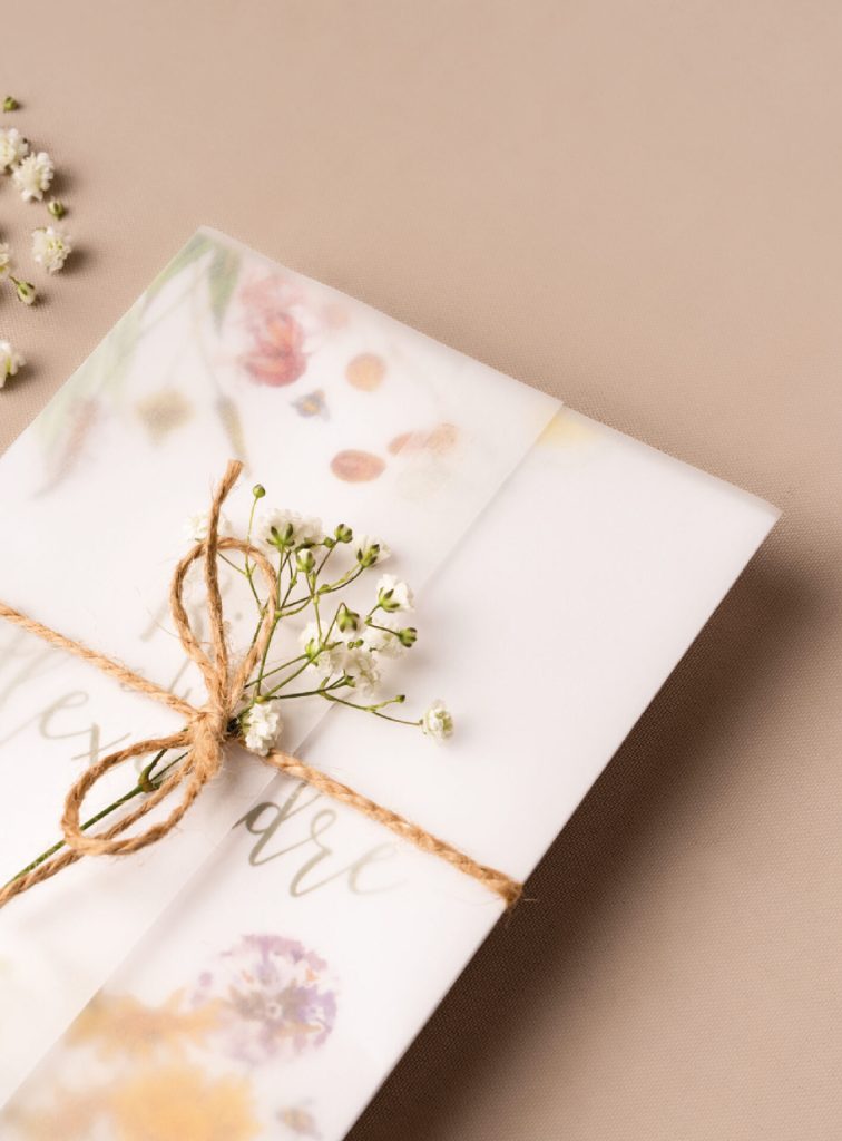 Convite de Casamento branco de estilo floral com letering verde e com ilustração de flores de varias cores com um envelope de papel vegetal